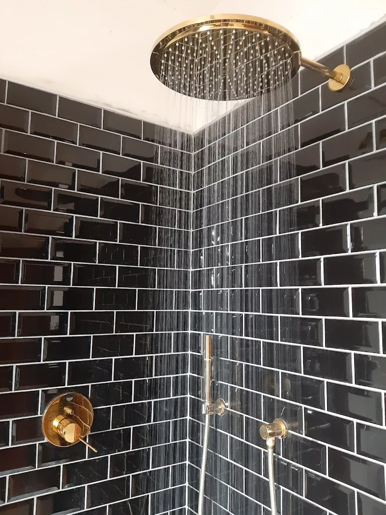 Douche à l'italienne carrelée en métro noir avec pomme de pluie dorée, réalisée par IDEP à Tournai
